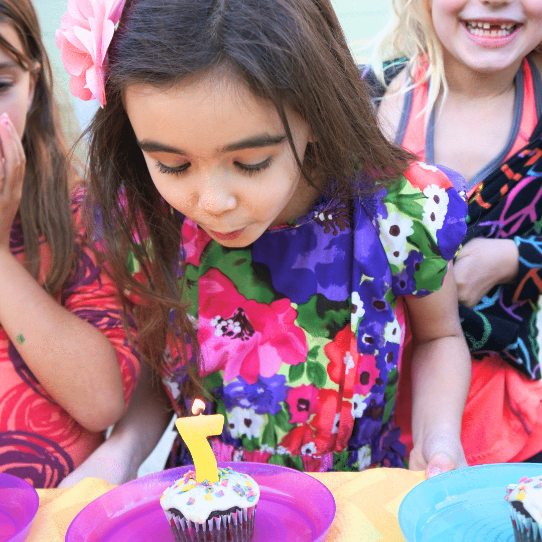 girl blowing out candles on a birthday cupcake